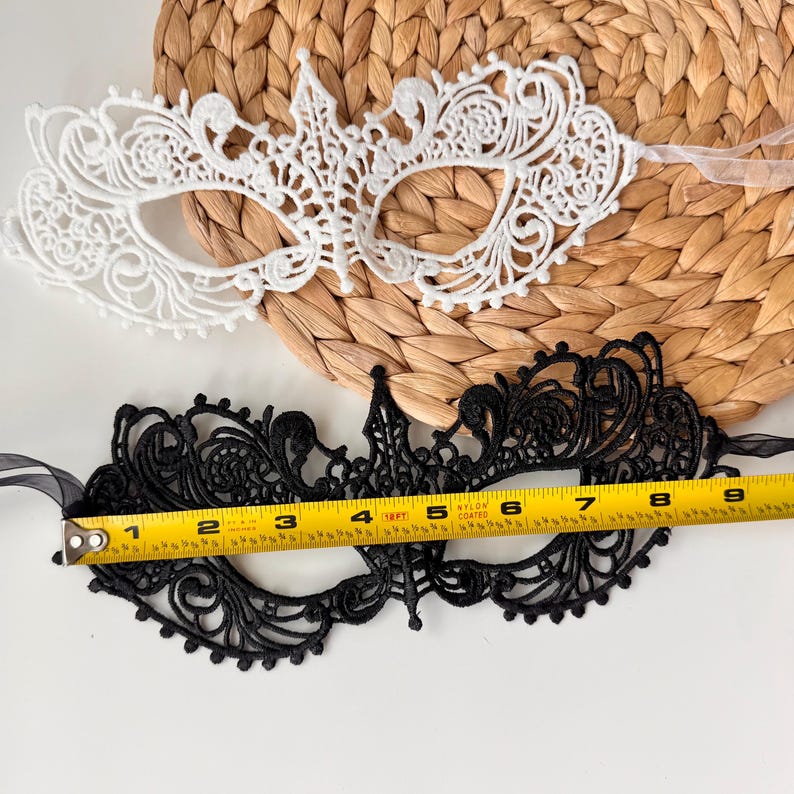 May include: Two lace masquerade masks. One is white, the other is black. The black mask is approximately 8 inches long. Both masks have intricate floral and scrollwork designs, with ribbon ties for securing them.