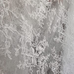 May include: White lace fabric with a delicate floral pattern. The lace is intricate and has a soft, flowing texture.