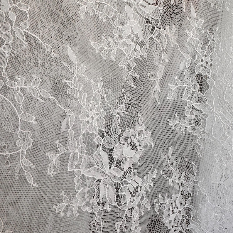 May include: White lace fabric with a delicate floral pattern. The lace is intricate and has a soft, flowing texture.