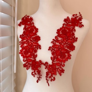 May include: Two red floral lace appliques, each with a symmetrical design of flowers and leaves. The appliques are displayed on a white mannequin, showcasing the intricate details and vibrant color.