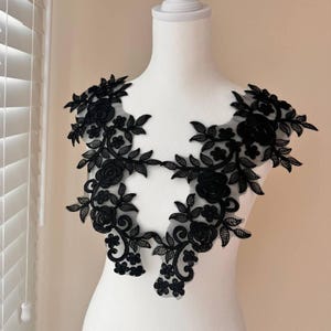 May include: Black floral lace applique with a delicate design featuring intricate leaves and flowers. This lace trim is perfect for adding a touch of elegance to any garment or craft project.