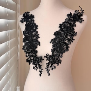 May include: Two black lace appliques, each featuring a floral design with roses and intricate detailing. The appliques are displayed on a mannequin, showcasing their shape and texture. Perfect for embellishing garments or crafts.