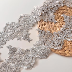 May include: Silver lace trim with floral and beaded details. The delicate trim features a scalloped edge and is ideal for embellishing garments, accessories, or home decor projects. The intricate design adds a touch of elegance and sophistication.