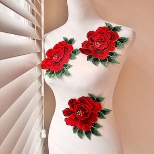 May include: Three red fabric flower appliques with green leaves. The flowers have a 3D effect and are embellished with small rhinestones.