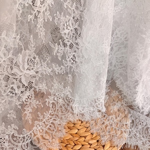 May include: White lace fabric with a delicate floral pattern. The lace is soft and sheer, with a subtle shimmer. It is perfect for adding a touch of elegance to any project.
