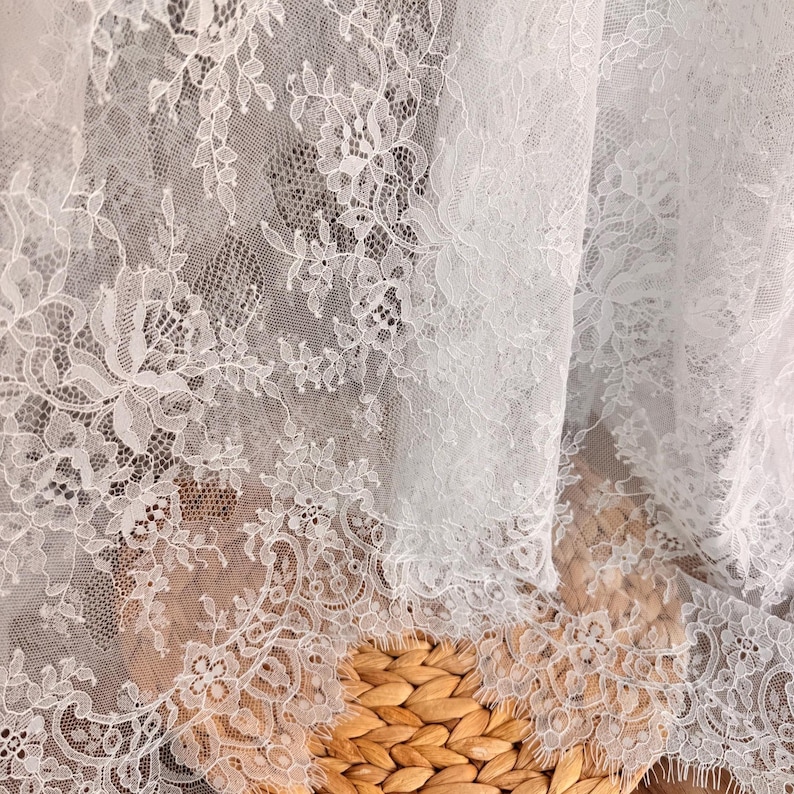 May include: White lace fabric with a delicate floral pattern. The lace is soft and sheer, with a subtle shimmer. It is perfect for adding a touch of elegance to any project.