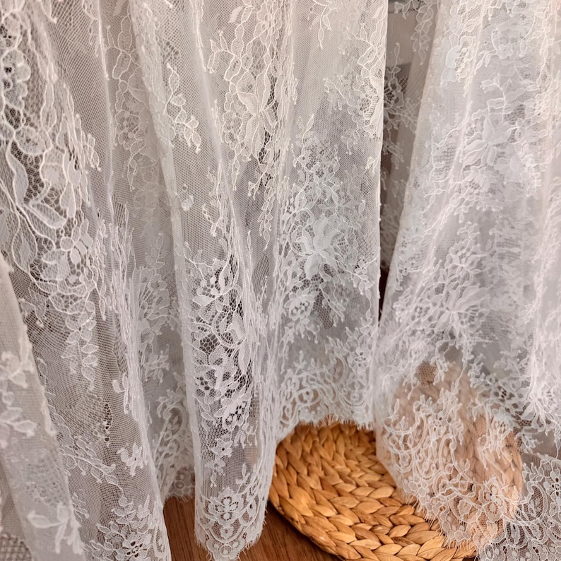 May include: White lace fabric with a delicate floral pattern. The lace is soft and sheer, with a delicate texture.