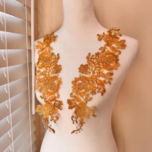 May include: Two golden-yellow floral lace appliques, each featuring intricate rose and leaf designs. The appliques are displayed on a white mannequin, showcasing their delicate details and potential for embellishment in garment design or craft projects.