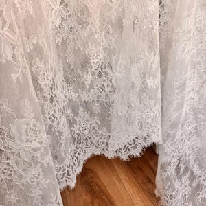 May include: White lace fabric with a delicate floral pattern. The lace has a scalloped edge.