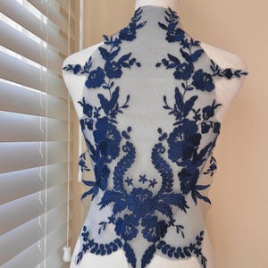 May include: Navy blue floral lace applique with intricate embroidered flower and leaf details. The applique is displayed on a mannequin, showcasing its design and texture. Perfect for embellishing garments or craft projects.