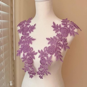 May include: A pair of mauve floral lace appliques with a delicate floral design. The appliques are perfect for adding a touch of elegance to any garment.
