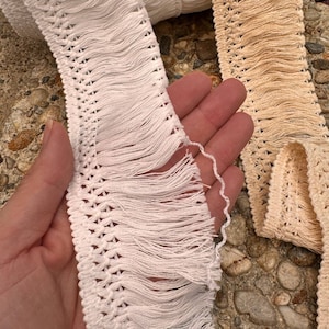 May include: Two spools of white and beige fringe trim with a crocheted design. The fringe is about 1 inch long.