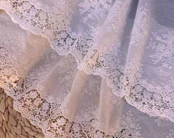 May include: White cotton fabric with delicate floral embroidery and a lace trim. The fabric is layered and the lace trim is visible on both layers.