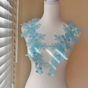 May include: Two light blue floral lace appliques with a delicate floral design. The appliques are perfect for adding a touch of elegance to any garment or project.