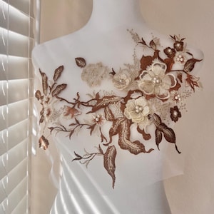 Può includere: Un'applicazione floreale delicata con ricami marroni e beige e dettagli di perle. L'applicazione è perfetta per aggiungere un tocco di eleganza a vestiti, accessori o arredamento per la casa.