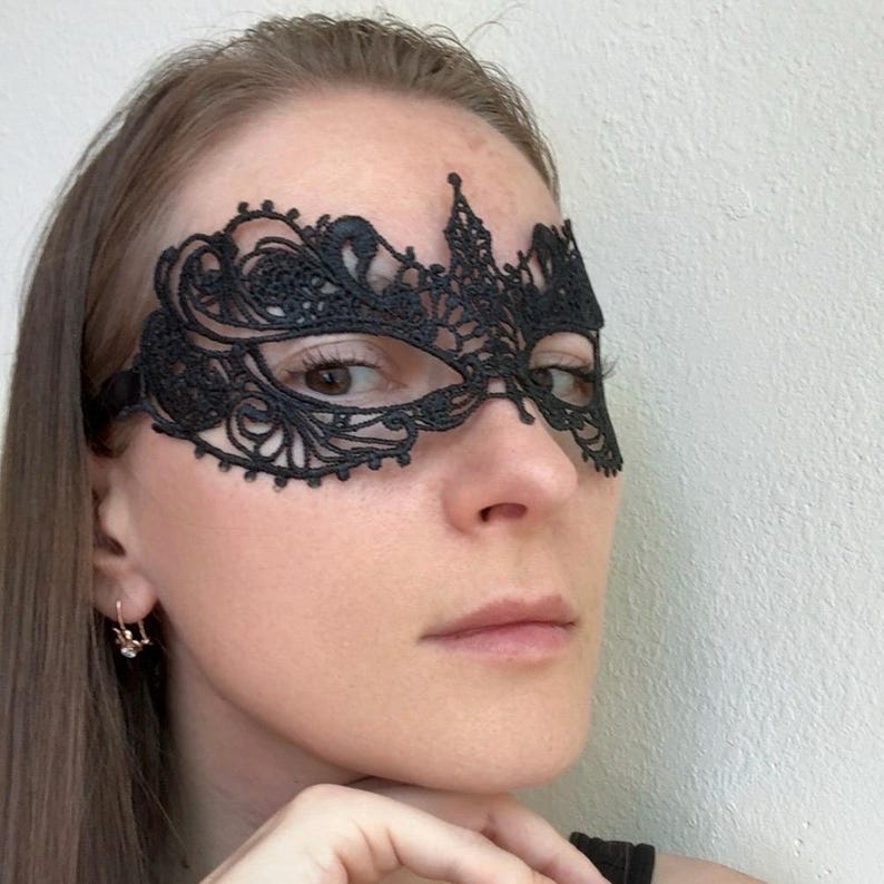 May include: Black lace eye mask with an intricate floral design. The mask covers the eyes and features a delicate, ornate pattern. A black elastic band secures the mask. Perfect for masquerade balls or costume parties.