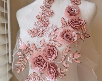 May include: A delicate rose applique with sequins and beads in a blush pink color. The applique features a cluster of roses and leaves, perfect for adding a touch of elegance to clothing or crafts.