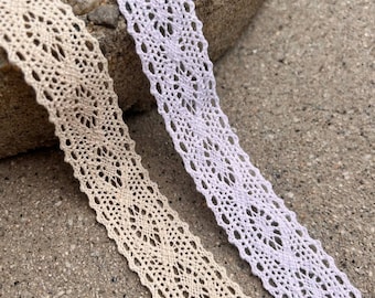 May include: Two spools of delicate lace trim, one in a light beige color and the other in a pale lavender color. The lace has a delicate floral pattern.