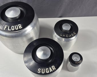 Juego de 4 botes de aluminio hilado plateado Kromex con tapa de baquelita negra y plateada estilo retro.