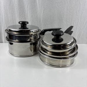 May include: A set of stainless steel cookware featuring a large pot with a lid and a smaller saucepan with a lid. Both pieces have black plastic handles and black knobs on the lids. The metal surfaces are reflective and polished in appearance.