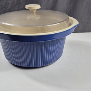 May include: A blue and beige casserole dish with a clear lid. The dish has a ribbed design on the exterior and a handle on the lid. The lid is clear, allowing a view of the contents.