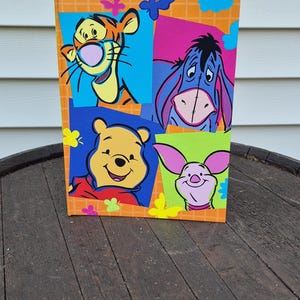 May include: A rectangular book with an orange grid background featuring colorful illustrations of Tigger, Eeyore, Winnie the Pooh, and Piglet. The cover is decorated with small blue, yellow, and pink butterfly shapes surrounding the four characters.