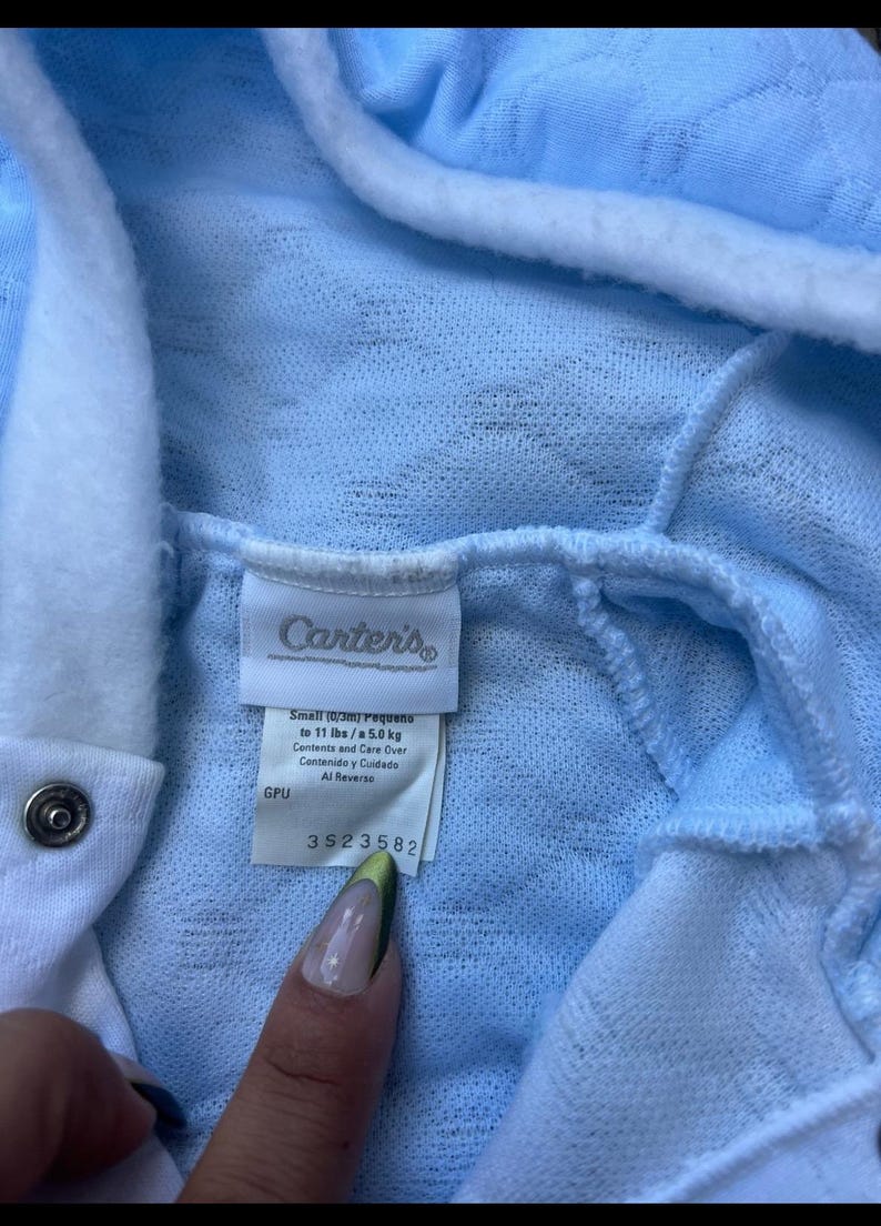 Puede incluir: Prenda de beb&eacute; azul claro con ribete y capucha blancos. La etiqueta dice "Carter's" e incluye informaci&oacute;n de talla: Peque&ntilde;o (0/3m) hasta 5,0 kg. La prenda tiene un cierre de bot&oacute;n a presi&oacute;n. La etiqueta tambi&eacute;n incluye el n&uacute;mero 3523582.