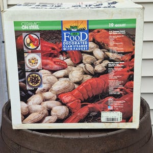 May include: A 19 quart Sea Food Decorated Clam Steamer with Faucet box featuring a graphic of a lobster and clams. The packaging includes text labels for lobster, clams, and mussels, with Ceramic on Steel branding and a 19 quart capacity label.