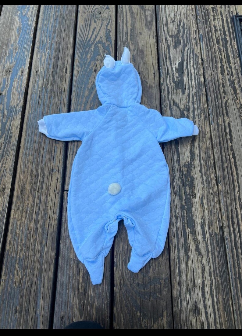 Puede incluir: Un disfraz de conejito para beb&eacute; en azul claro con un dise&ntilde;o acolchado. El mono con capucha presenta orejas de conejo blancas, pu&ntilde;os blancos y una cola blanca y esponjosa. Para beb&eacute;s y ni&ntilde;os peque&ntilde;os.