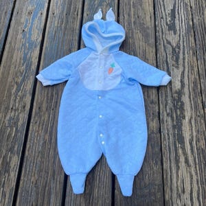 Puede incluir: Traje de conejito acolchado azul para beb&eacute; con capucha y orejas adjuntas. El traje tiene un babero blanco con una aplicaci&oacute;n de zanahoria y cierres de bot&oacute;n. El atuendo est&aacute; dise&ntilde;ado para beb&eacute;s y est&aacute; hecho de un material suave y c&oacute;modo.