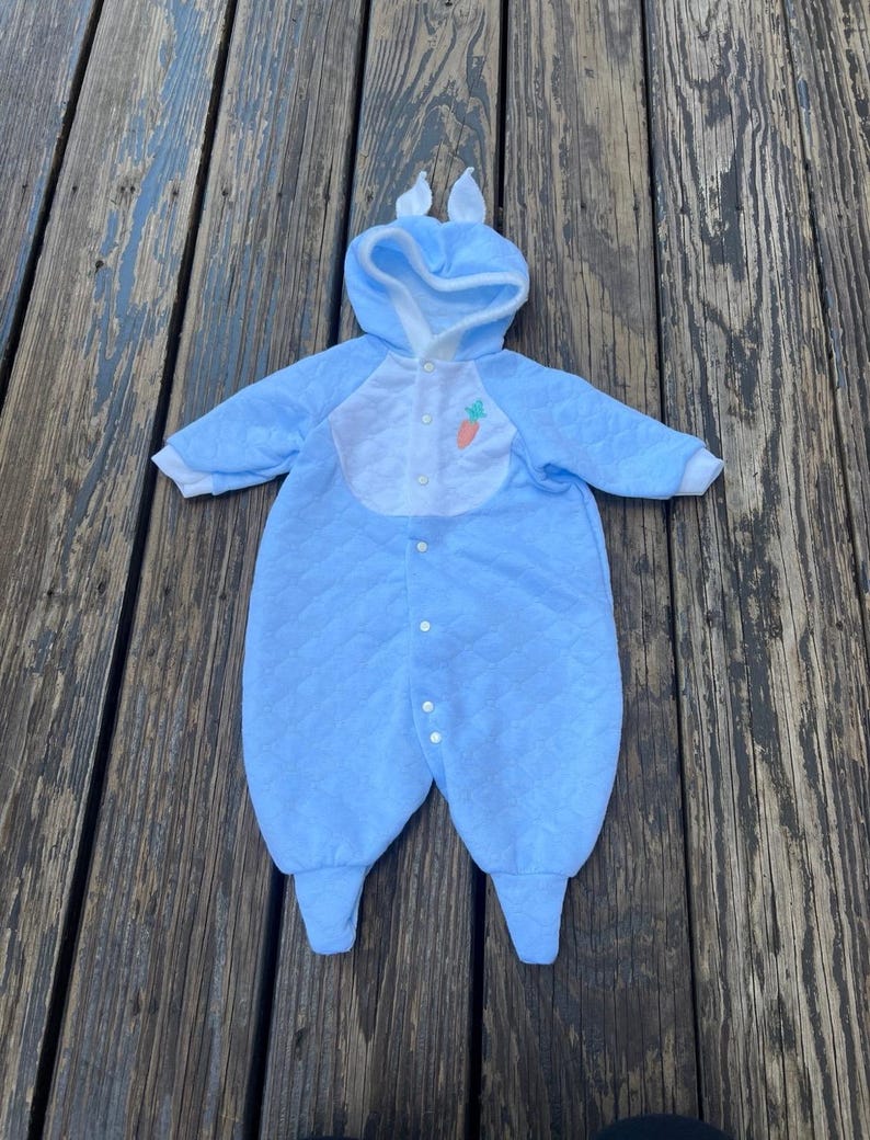Puede incluir: Traje de conejito acolchado azul para beb&eacute; con capucha y orejas adjuntas. El traje tiene un babero blanco con una aplicaci&oacute;n de zanahoria y cierres de bot&oacute;n. El atuendo est&aacute; dise&ntilde;ado para beb&eacute;s y est&aacute; hecho de un material suave y c&oacute;modo.