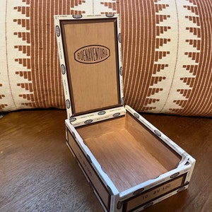 Może przedstawiać: Puste drewniane pudełko na cygara z białą etykietą, na której widnieje napis "Buena Ventura" i "10 BV 500".