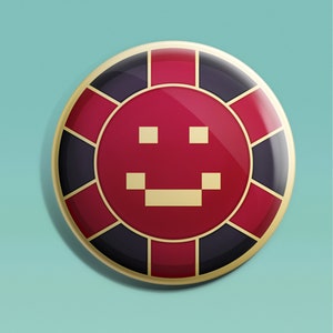 May include: A red and black casino chip with a gold border and a pixelated smiley face in the center.