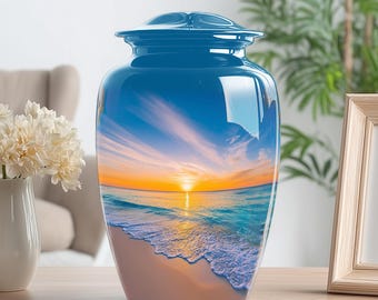 May include: A blue cremation urn with a glossy finish. The urn features a scenic image of a beach at sunset, with the sun setting over the ocean. The urn is sitting on a wooden surface.