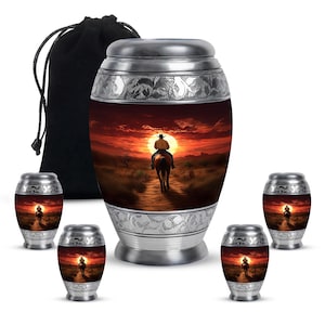 May include: A set of five silver urns featuring a cowboy riding a horse at sunset design. The urns are in different sizes and come with a black velvet bag.