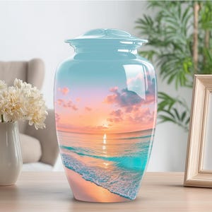 May include: A light blue cremation urn with a glossy finish. The urn features a scenic beach sunset design with a vibrant sky, ocean, and sandy shore. The urn is a decorative memorial for a loved one.