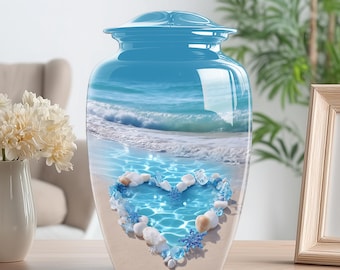 May include: A blue cremation urn with a glossy finish. The urn features a beach scene with a heart-shaped arrangement of shells and blue accents. The urn is sitting on a wooden surface.