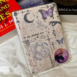 May include: A clear phone case with a whimsical design featuring a purple butterfly, a crescent moon, a sun, a sword, and the text "In my fantasy era".