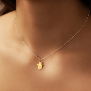 May include: A silver chain necklace with a gold hamsa hand pendant. The hamsa hand is a symbol of protection and good luck.