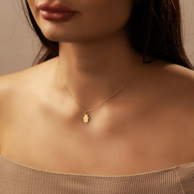 May include: A gold chain necklace with a hamsa hand pendant. The hamsa hand is a symbol of protection and good luck.