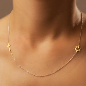 Może przedstawiać: Delikatny złoty naszyjnik z łańcuszkiem, z małym wisiorkiem w kształcie krzyża po jednej stronie i wisiorkiem w kształcie Gwiazdy Dawida po drugiej.