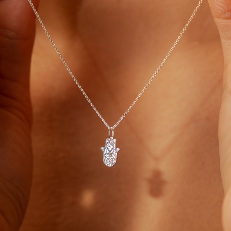 May include: A silver chain necklace with a hamsa hand pendant. The hamsa hand is a popular symbol of protection and good luck.