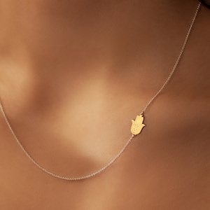 May include: A delicate gold chain necklace with a hamsa hand charm. The hamsa is a symbol of protection and good luck.