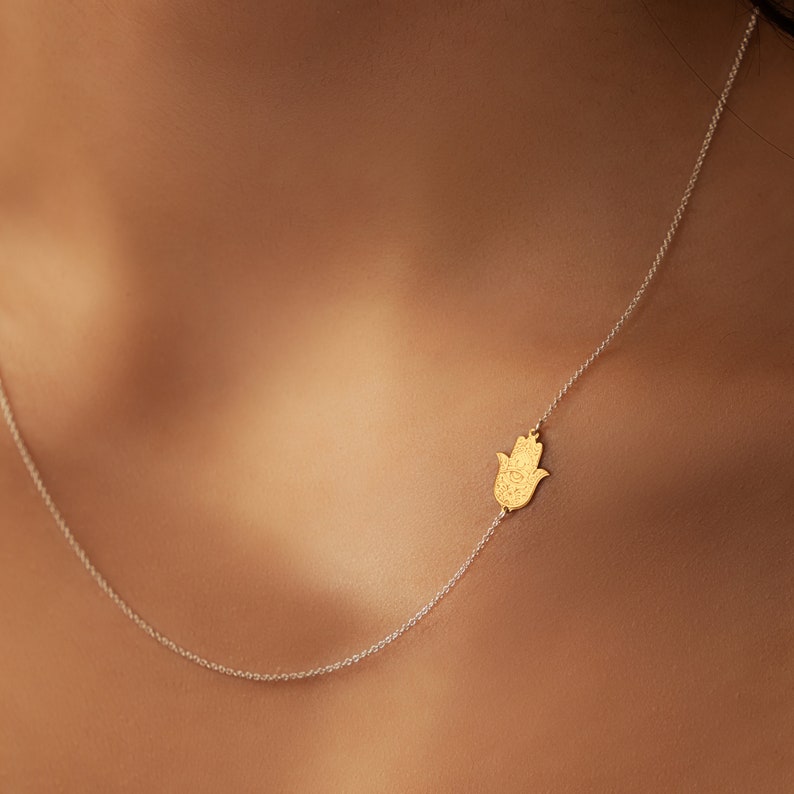 May include: A delicate gold chain necklace with a hamsa hand charm. The hamsa is a symbol of protection and good luck.
