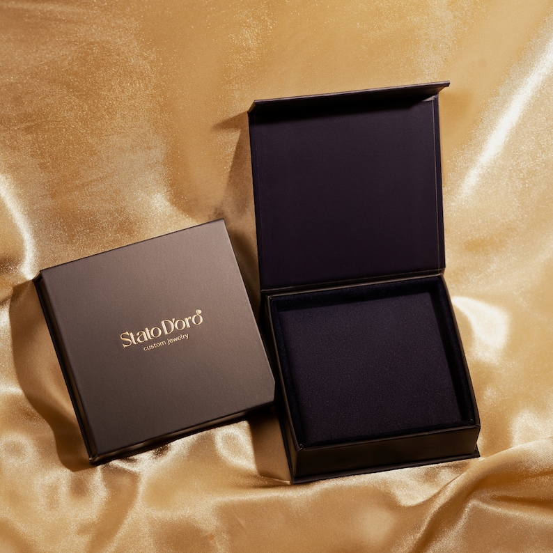 May include: Two black boxes with a gold logo that reads "Stato D'oro custom jewelry". The box on the right is open, revealing a black velvet interior.