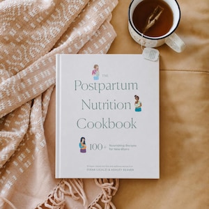 May include: A white cookbook titled "The Postpartum Nutrition Cookbook" with text and illustrations, next to a mug of tea and a beige blanket. The book cover features the title in green and the subtitle "Nourishing Recipes for New Moms".