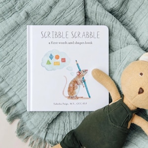 May include: A square hardcover book titled Scribble Scrabble: a first words and shapes book by Tabitha Paige, M.S., CCC-SLP. The white cover features a watercolor illustration of a brown mouse holding a blue pencil with a thought bubble of shapes.