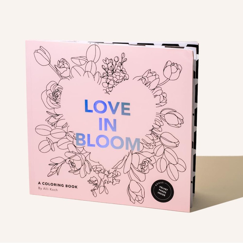 May include: A pink coloring book titled "LOVE IN BLOOM" with a floral heart design. The book includes the text "A COLORING BOOK By Alli Koch" and a bonus "VELVET PAGES INSIDE" sticker. The book's spine has a black and white pattern.
