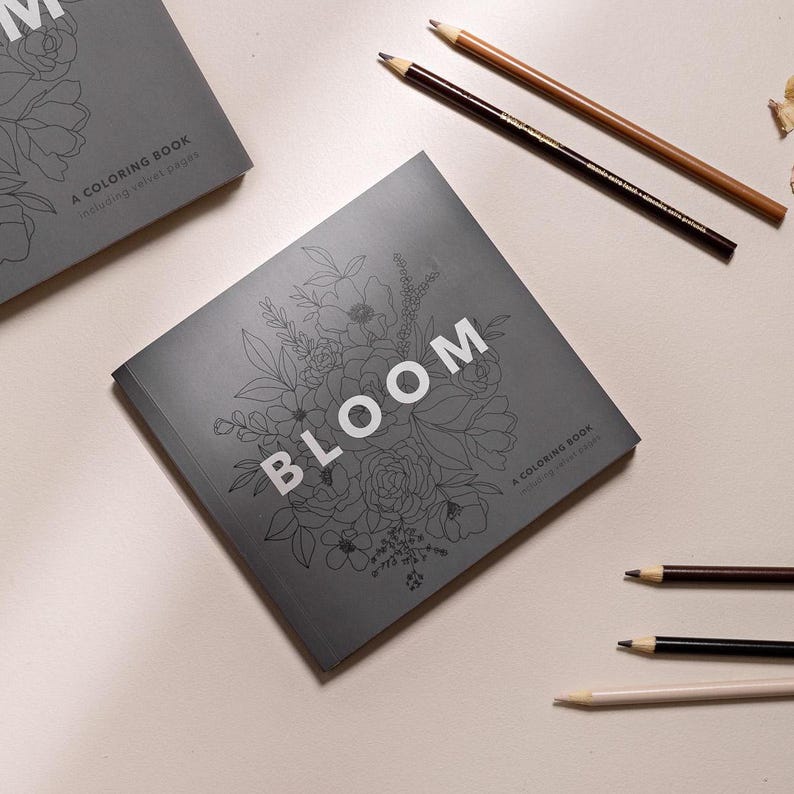 May include: A gray coloring book with a floral design and the word "BLOOM" in white text. The book is titled "A Coloring Book featuring vibrant pages".