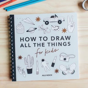 May include: A spiral-bound instructional drawing book titled How to Draw All the Things for Kids by Alli Koch. The white cover features black line art illustrations of a truck, cupcake, cactus, camera, butterfly, and other objects, surrounded by colored pencils.